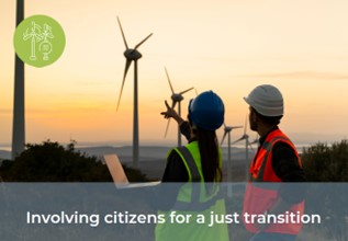 A man in an orange hi vis vest and white hardhat and a woman in a yellow hi vis vest and blue hardhat, holding a laptop and pointing to numerous large wind turbines in the distance.