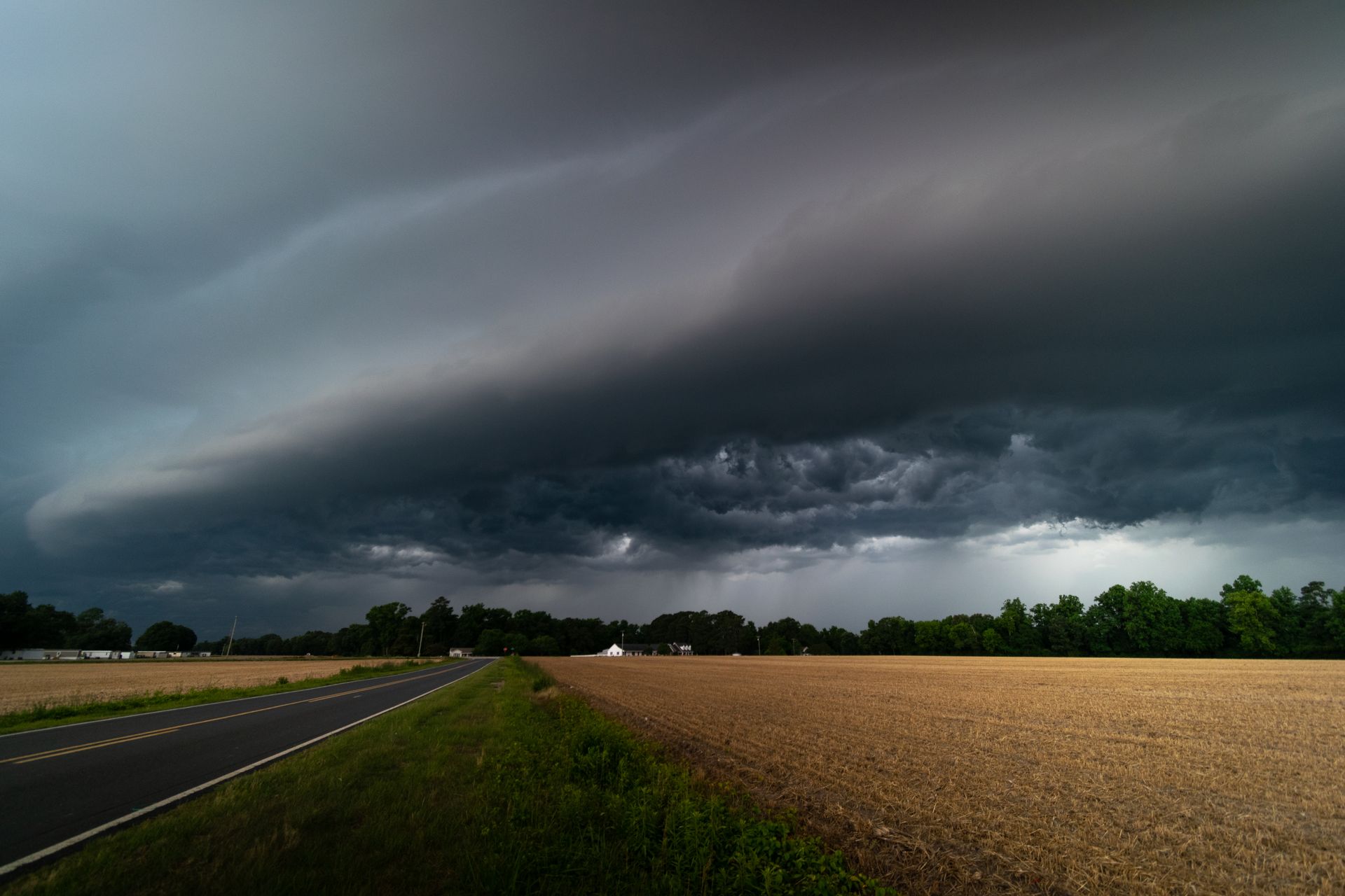 A mesmerizing view of dark storm clouds approaching over a rural road and farmland.